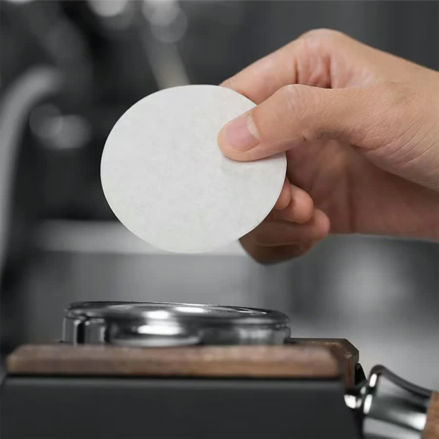 Hand legt ein rundes Filterpapier auf den Siebträger